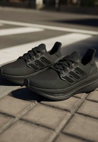 Двойка черни маратонки Adidas с мрежести горни части и "Light Boost" подметки, поставени на външен тротоар близо до пешеходни линии.