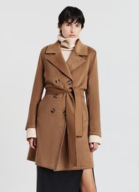 Cappotto marrone doppiopetto realizzato in materiale morbido. Caratterizzato da una cintura con fiocco, ampi revers e tasche laterali, abbinato a un dolcevita crema.