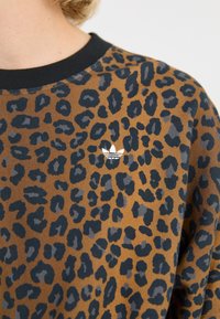 Brauner Pullover mit schwarzen Leopardenflecken, ausgestattet mit einem schwarzen Rundhalsausschnitt und einem kleinen weißen Trefoil-Logo auf der Brust.