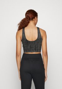 Top deportivo negro recortado con diseño de espalda redonda, que presenta un patrón de tie-dye texturizado. Combinado con leggings negros de cintura alta.