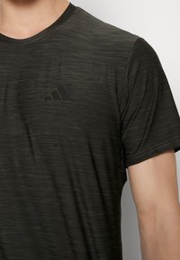 Tmavě šedé sportovní tričko s texturovanou tkaninou, kulatým výstřihem a krátkým rukávem. Obsahuje nenápadné černé logo na hrudi.
