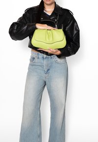 Limoengroene leren handtas met een zachte, gestructureerde oppervlakte en een ronde vorm, vastgehouden door een persoon in een zwart leren jack en lichte jeans.