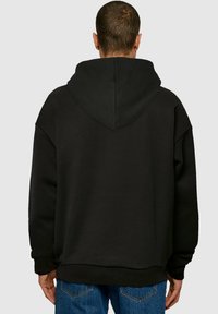 Svart oversized hettegenser med stor hette, teksturert stoff, senket skuldre og ribbestrikkede mansjetter og kant. Enkelt design uten grafikk.