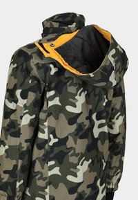 Kamouflagejacka med en blandning av gröna, bruna och beige mönster. Har ett svart foder och en gul accent inuti huvan.