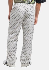 Pantalon blanc à motif avec un design subtil, présentant un mélange de logos. Fabriqué à partir d'un tissu lisse, avec une taille élastique et des poches latérales.