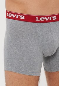 Sivi bombažasti bokserci z rdečim elastičnim pasom, na katerem je belo oznako "Levi's". Gladka tekstura in prilega se oblikam.