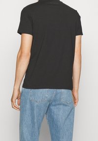 Camiseta de algodón negra con mangas cortas, que presenta un escote redondo y un corte relajado. Combinada con jeans de mezclilla azul claro.
