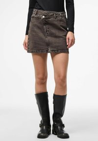 Frau trägt einen ausgebleichten schwarzen Denim-Minirock, ein schwarzes Langarmoberteil und schwarze Lederstiefel mit Schnallendetails bis zur Wadenmitte.