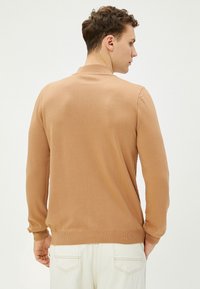 Lichtbruine gebreide pullover met lange mouwen en een geribbelde kraag. De achterkant heeft een gladde textuur en een eenvoudig, aansluitend ontwerp.