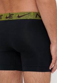 Fekete, rugalmas boxer alsónadrág sárga és barna mintás derékkal. Szoros illeszkedés és sima szövet jellemzi.