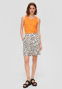 Pomarańczowy top bez rękawów zestawiony z białymi szortami w czarno-pomarańczowy wzór lamparta oraz czarnymi sandałami na paski z grubą podeszwą.
