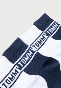 Άσπρες και ναυτικής μπλε κάλτσες με ριμπ ύφασμα στη μανσέτα που φέρει επαναλαμβανόμενο λογότυπο "TOMMY" σε ναυτικό μπλε κατά μήκος της άκρης της μανσέτας.