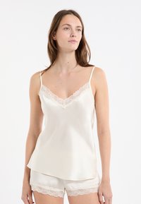 Jedwabny top na ramiączkach z koronkowym wykończeniem przy dekolcie, zestawiony z pasującymi jedwabnymi szortami z koronkowymi akcentami na końcach. Kolor: kremowy.