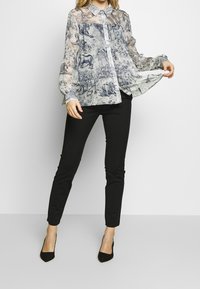 Genomskinlig blus i blå och vit mönster med djurmotiv, med manschetterade ärmar och knäppning; i kombination med svarta slim-fit byxor och klackar.