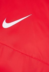El material atlético rojo presenta un logo blanco de Nike y un detalle de costura prominente. Textura suave con un diseño liviano.