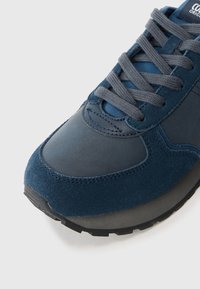 Marineblauwe sneaker met een mix van gladde en suède texturen, ronde neus, grijze veters en een rubberen zool met een uniek profiel.