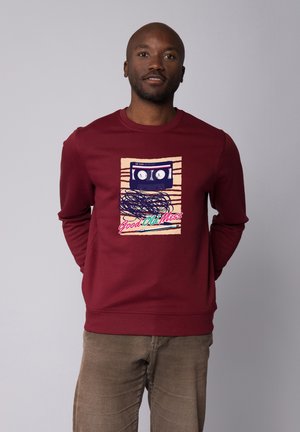 Bordeauxfarbener Hoodie mit einer Grafik eines Kassettenrecorders und einem verworrenen Banddesign. Rundhals, weicher Stoff und gerippte Bündchen.