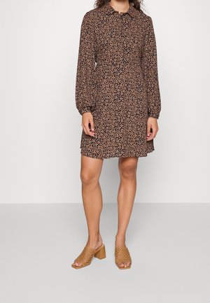 Vestito floreale nero con maniche lunghe e colletto, caratterizzato da piccoli fiori arancioni. Abbinato a sandali con tacco marroni con un design a taglio.