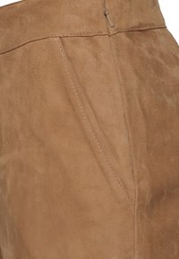 Bruine suede stof met een gladde textuur, met zichtbare naden en een discrete ritsdetail aan de zijkant.