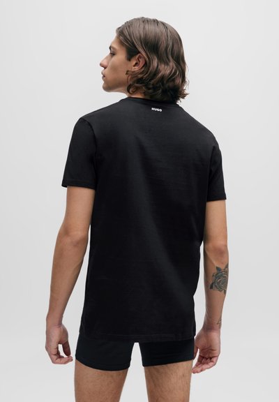 T-shirt en coton noir à manches courtes, avec un col rond et le logo "HUGO" au dos. Texture lisse et coupe décontractée.
