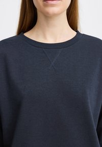 Mørkeblå crewneck sweatshirt lavet af blødt stof, med en tekstureret krave og en X-syning detalje ved kraven.