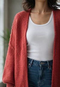 Miękki, puszysty kardigan w kolorze rdzy, nałożony na białą, prążkowaną tank top, zestawiony z dżinsami z wysokim stanem. Widoczna miękka faktura.