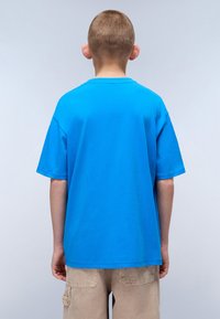 Blue cotton t-shirt with short sleeves and a round neckline, seen from the back. Smooth texture, relaxed fit, and clean stitching details.