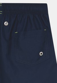Calções azul marinho com cintura elástica, apresentando um bolso traseiro com um ilhó prateado e um detalhe de costura verde em contraste.