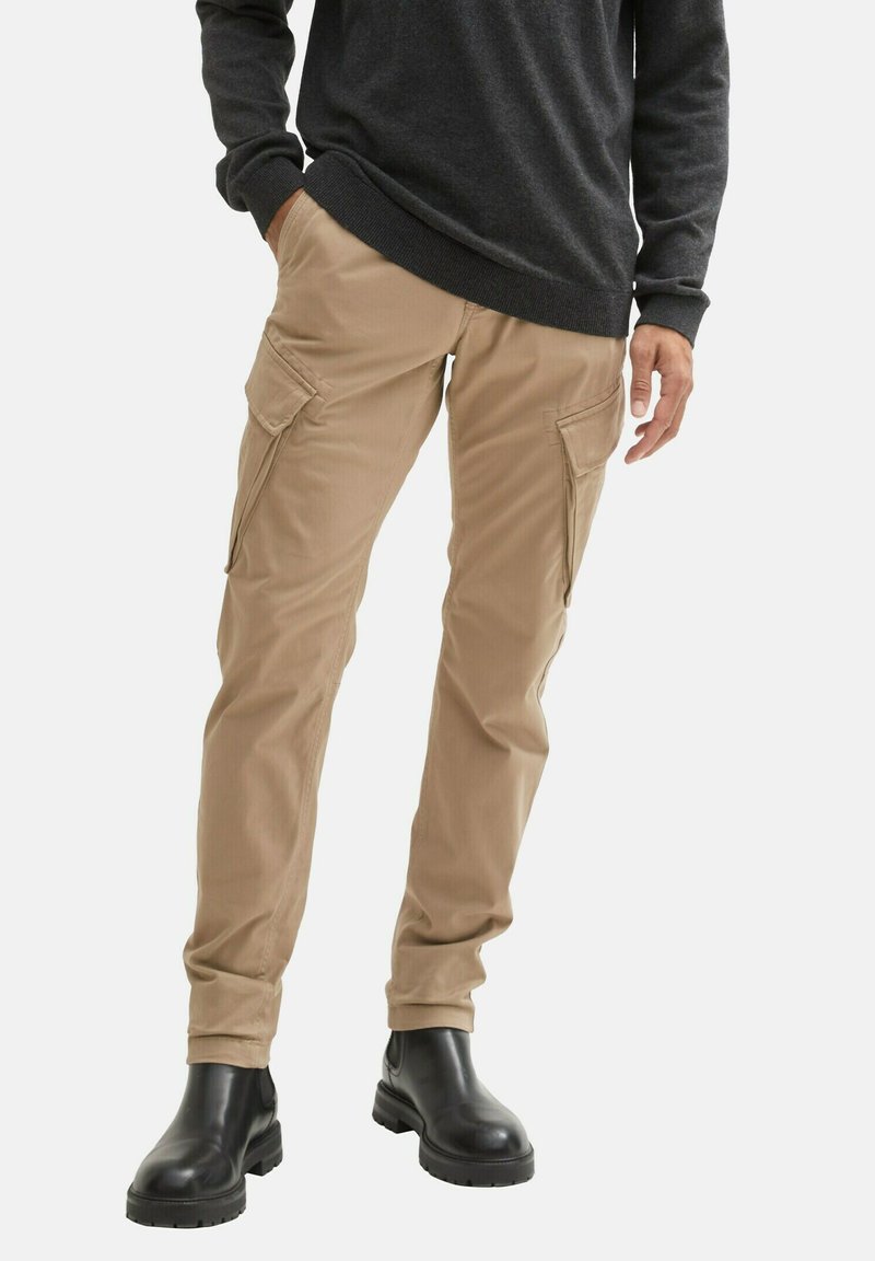 Beige Cargo-Hosen aus weichem Stoff, mit mehreren Seitentaschen, schmaler Passform und kombiniert mit schwarzen Stiefeletten.