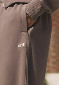 Brune sweatpants med en blød tekstur, der har en sidelomme og broderet "self." logo. Ribbet talje giver ekstra detaljer.