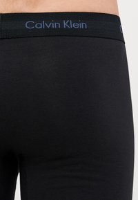 Fekete pamut boxer alsónemű egyszínű kivitelben, elasztikus derékpánttal, kék "Calvin Klein" felirattal.
