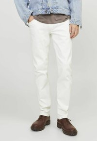 Jeans in denim bianco con vestibilità slim, abbinati a una camicia grigia e a una giacca di denim azzurro chiaro. Completati da scarpe stringate marroni.