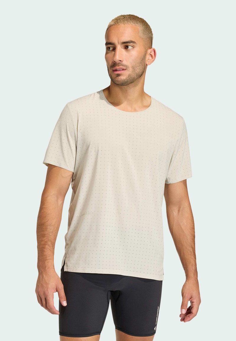 Μπεζ κοντομάνικο μπλουζάκι με διακριτό πουά μοτίβο, στρογγυλή λαιμόκοψη και πλαινές σχισμές, συνδυασμένο με μαύρες αθλητικές βερμούδες. Μαλακή υφή υφάσματος.