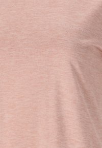 Ljust rosa, mjukt tyg med en melerad textur. Har en subtil logotyp på bröstet. Klassisk t-shirtform med rund nacke.