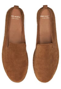 Des chaussures en daim marron à enfiler avec une texture lisse, de légers détails de couture et un bout arrondi, étiquetées "FRED MARTIN FABRIQUÉ EN ESPAGNE."