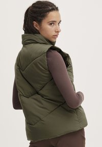 Gilet matelassé vert olive avec un col montant, présentant un motif en losanges, en matériau léger et sans quincaillerie visible.