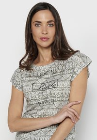 Camiseta gris con estampado de patrones, de manga corta, que presenta diseños geométricos y textos en negro. Tejido suave y ajuste relajado.
