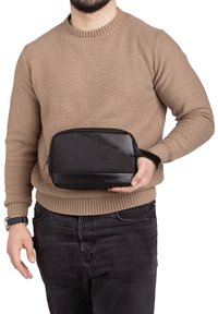 Zwarte toilettas met een gestructureerd bovenpaneel en een glad onderpaneel, ritssluiting en een polsband voor gemakkelijke draagbaarheid.