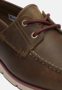 Bruna läderskärgårdsskor med rund tå, guldtonade öglor, vinröda snören och beige gummisula med en texturerad finish.