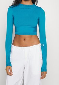 Blå kortärmad topp med ribbad struktur, rund hals och kontrasterande sömmar. Bärs med vita byxor med dragsko.