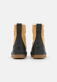 Brune suede støvler med sorte gummisåler, med en uldforing og sorte detaljer på hælen. Logo vist på siden.