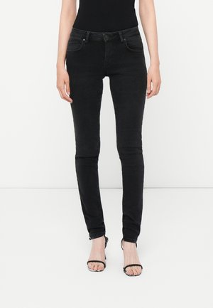 Fekete denim nadrág szűk szabással, öt zsebes kialakítással, gombos záródással és övhurkokkal, fekete magassarkú szandálokkal párosítva.