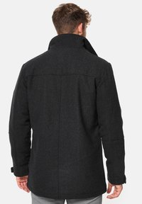 Abrigo de lana negro con cuello alto, hombros estructurados y dos bolsillos laterales, con una textura suave y detalles de costura mínimos.