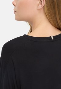 Schwarzes Shirt mit glatter Textur, entspannter Passform und einem subtilen Akzent am hinteren Ausschnitt mit einem kleinen gestreiften Detail.