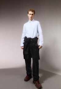 Lichtblauw overhemd met lange mouwen, zwarte corduroy broek en bruine sneakers. Het overhemd om de taille gebonden voegt detail toe.