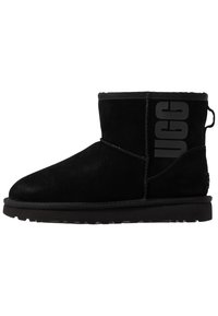 Černá semišová kotníková bota s kulatou špičkou, s tlustou černou podrážkou a výrazným potiskem loga na vn�ější straně. Měkká textura.