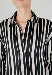 Camicia a righe bianco e nero con colletto a punta, caratterizzata da una texture morbida e bottoni neri lungo la parte anteriore.