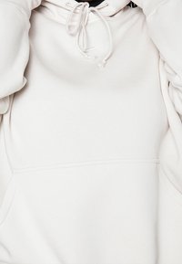 Světlobéžová mikina vyrobená z měkké tkaniny. Obsahuje přední kapsu, kapuci se šňůrkou a žebrované manžety. Minimalistický design bez vzorů.