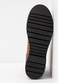 Semelle d'une chaussure marron présentant une bande de roulement en caoutchouc noir avec la marque "TOMMY JEANS" et la taille 37 embossée sur la semelle.