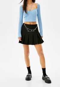 Světle modrý žebrovaný crop top s dlouhými rukávy, spárovaný s černou skládací sukní se stříbrným řetízkem.